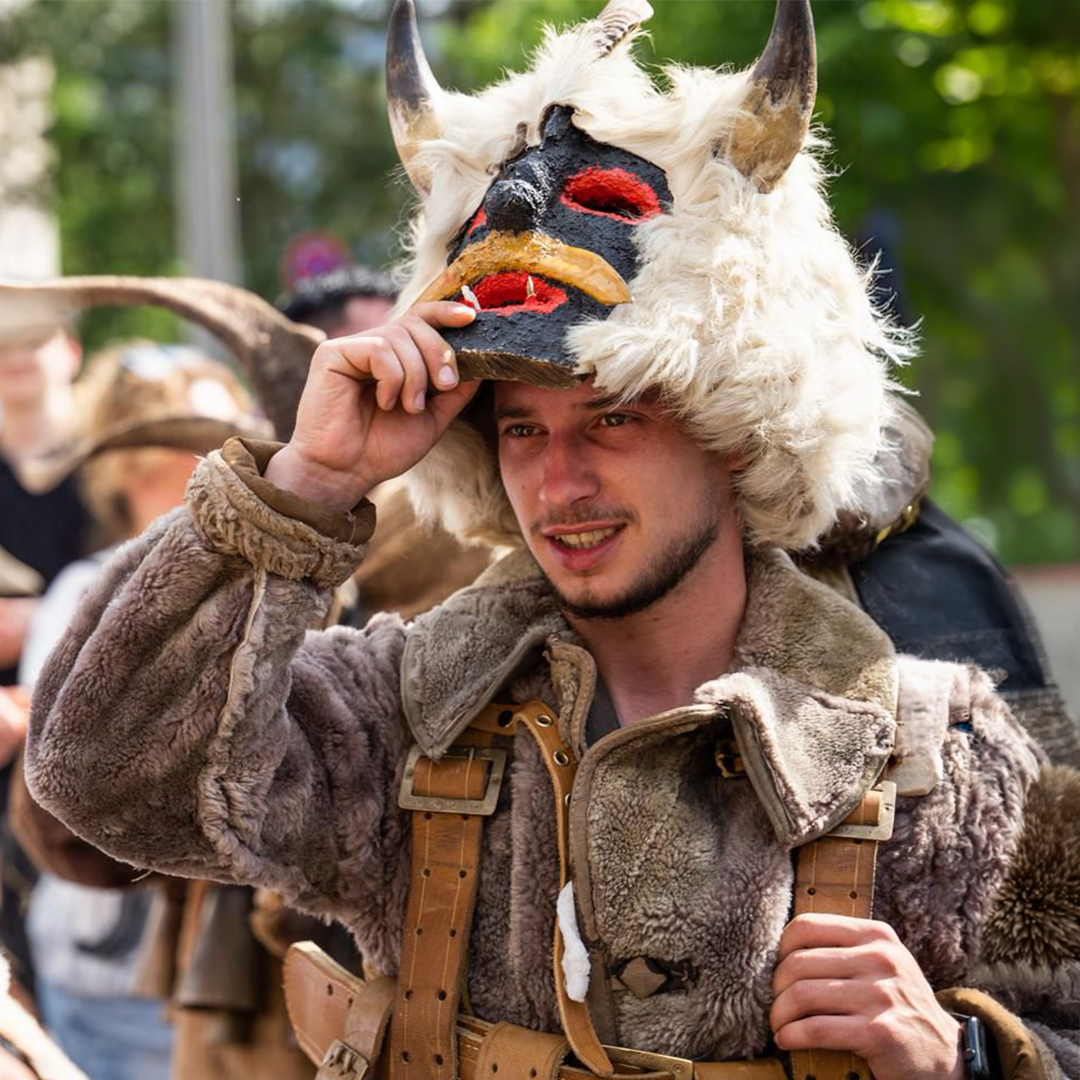Young Kuker performer lifting a horned wooden mask with white fur